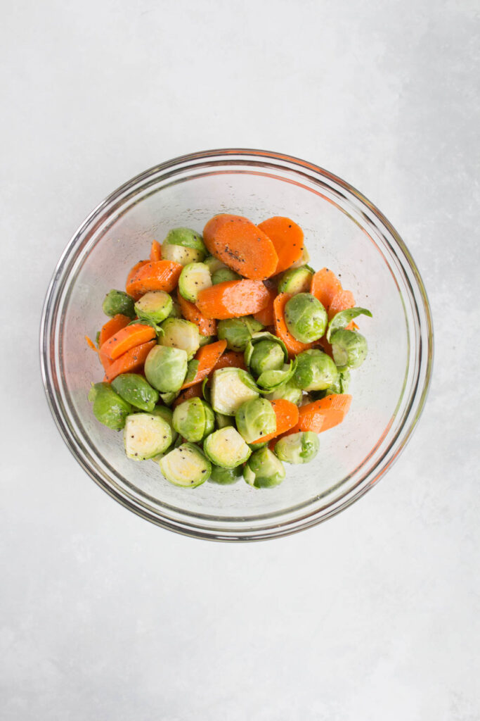 A bowl of seasoned and oiled brussels sprouts and carrots.