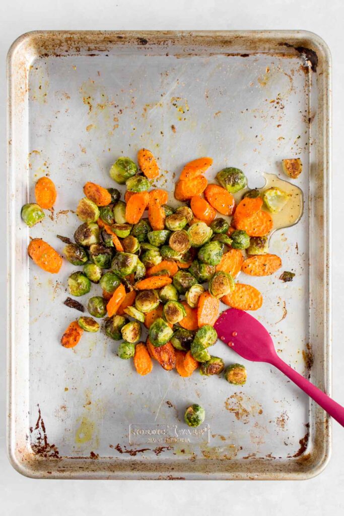 A pan of roasted brussels sprouts and carrots with maple syrup drizzled over top.