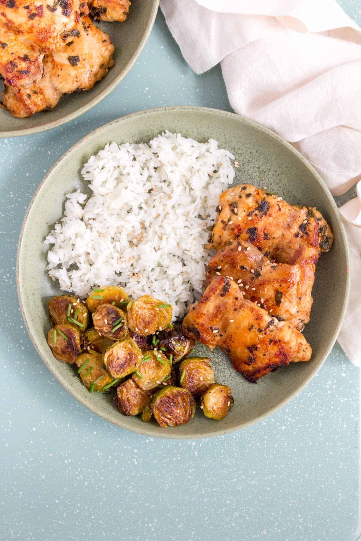 Three sage chicken thighs with rice and brussels sprouts in a green plate.