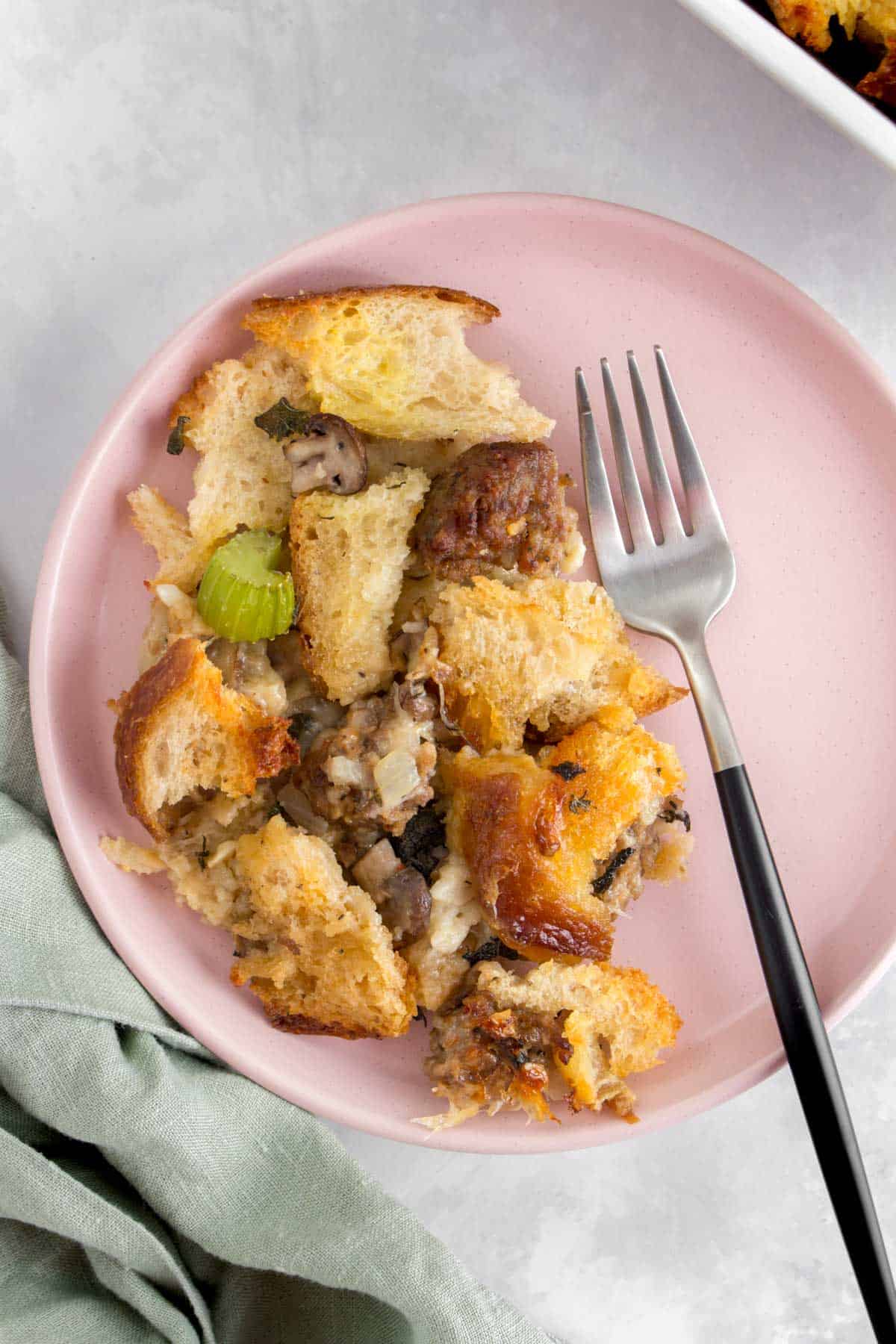 Close up of a plate of sourdough stuffing with pieces of sausage, mushrooms, and celery.