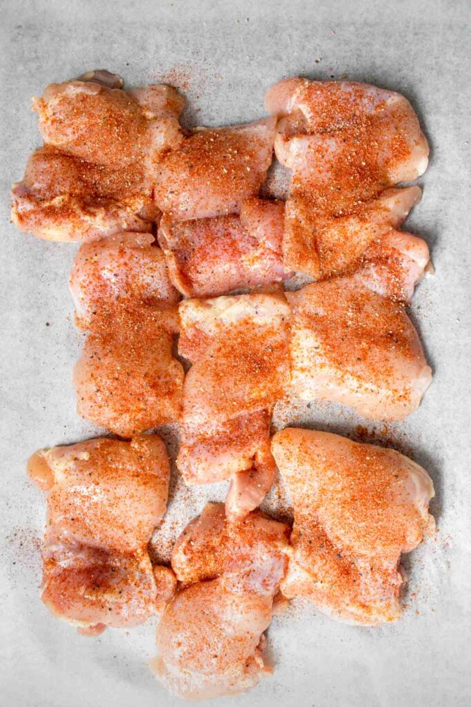 Chicken thighs being seasoned.