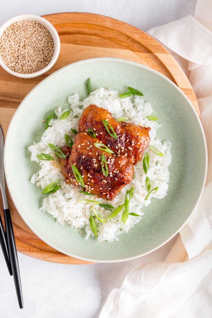 A plate of teriyaki chicken thighs with rice.