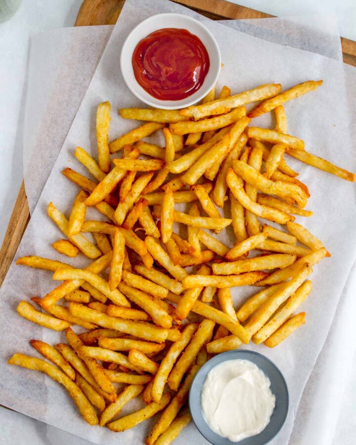 Air fryer frozen fries on a wooden serving board with dipping sauces.