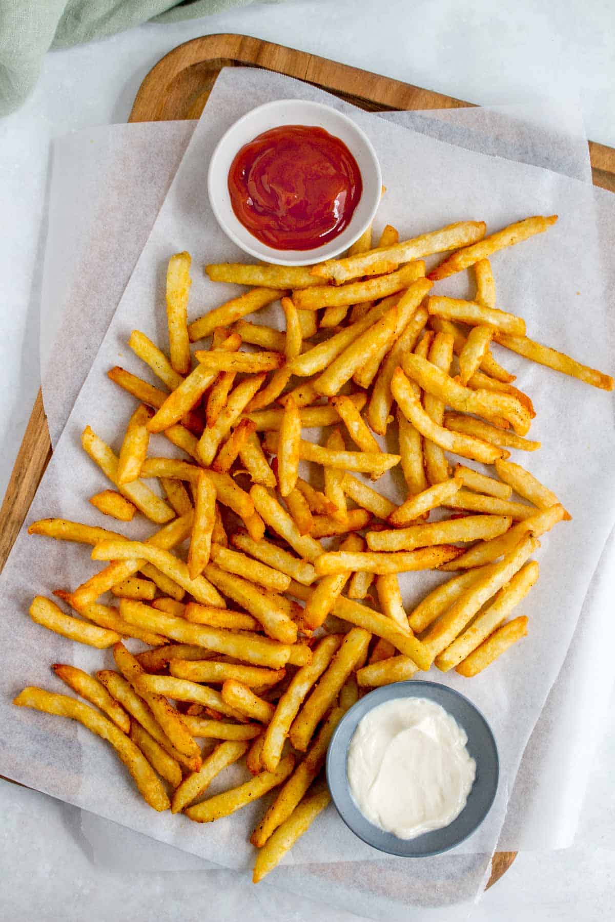 Air fryer frozen fries on a wooden serving board with dipping sauces.