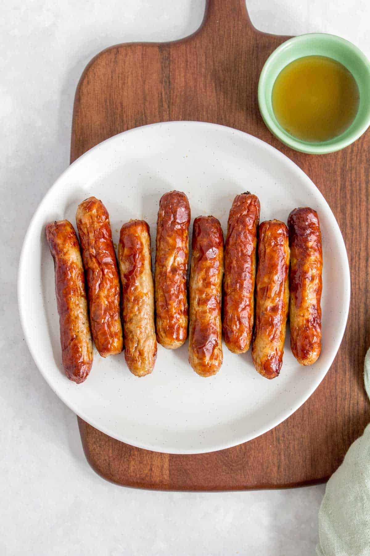 A plate with eight air fryer sausage with maple syrup on the side.