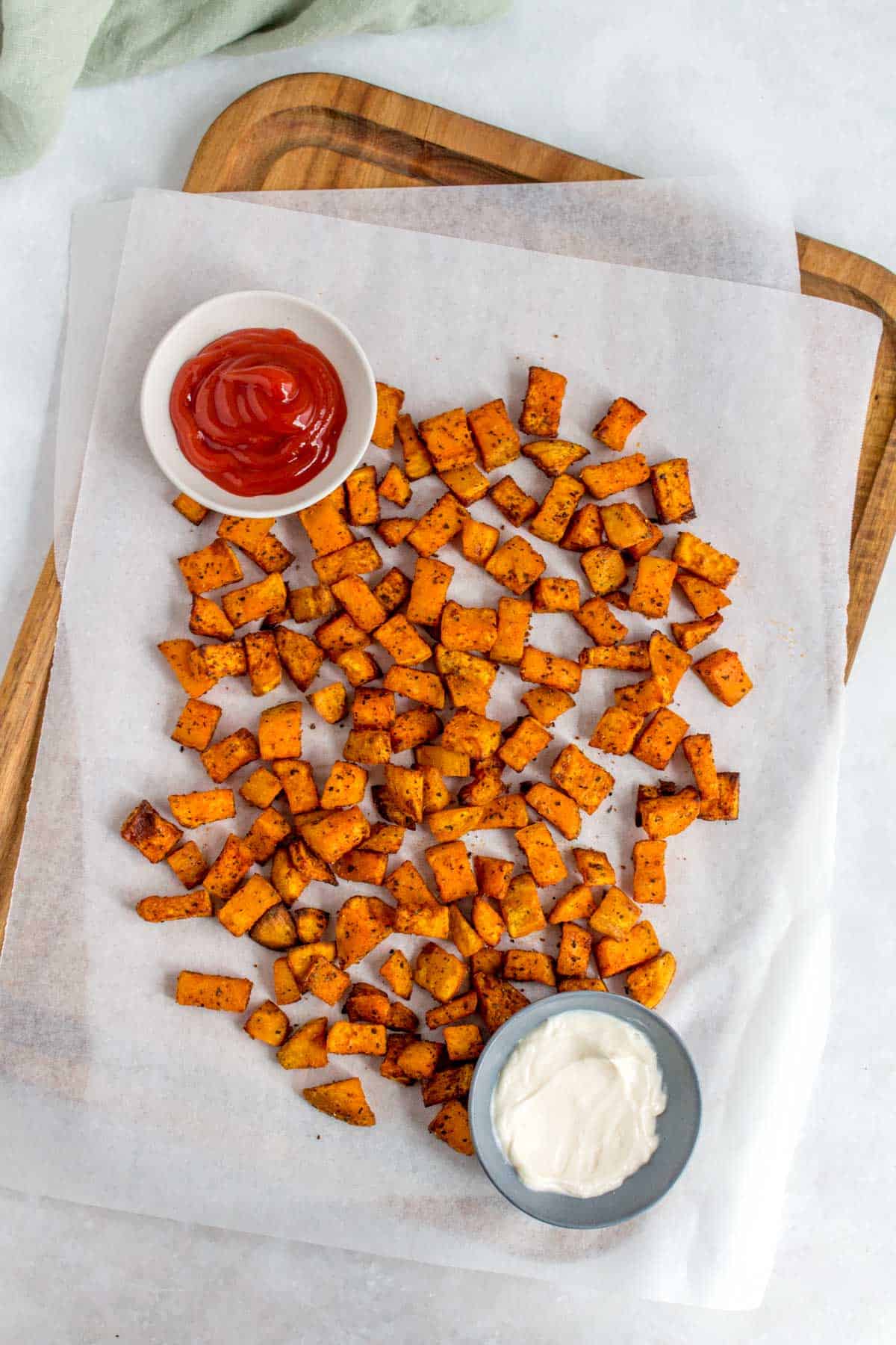 A wooden serving board with air fryer sweet potato cubes with dipping sauces.