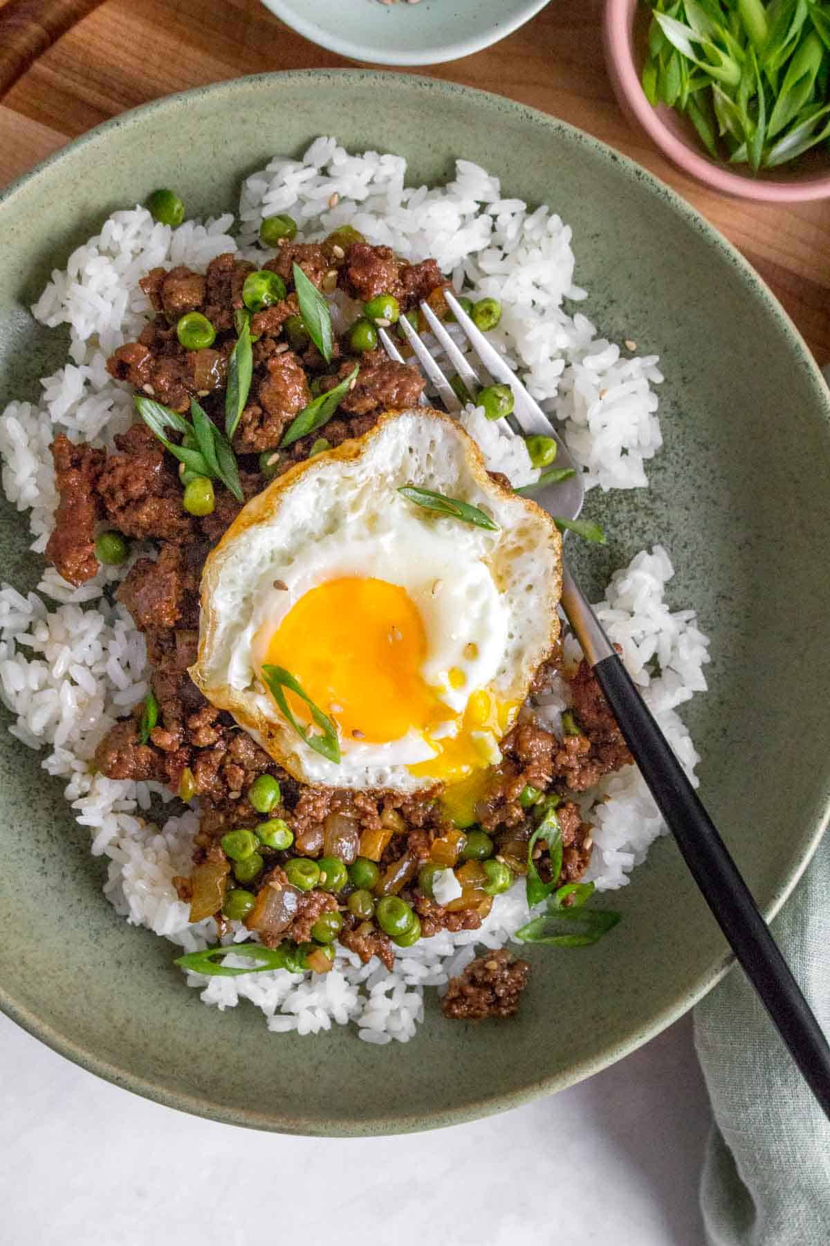 A bowl of rice with ground beef and fried egg on top with a fork inside.