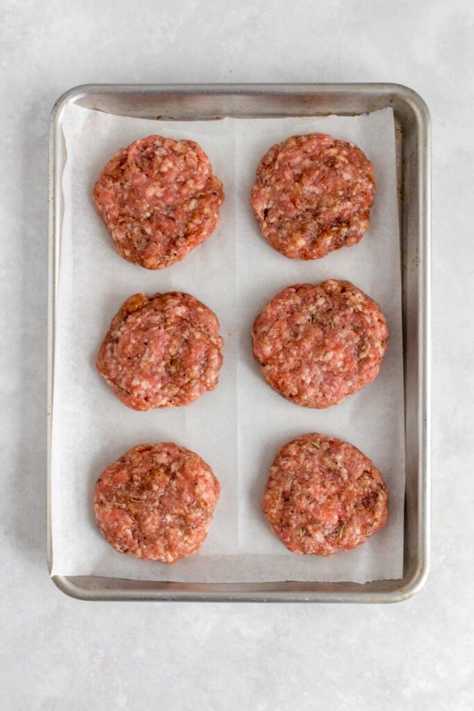 Six sausage patties shaped and formed on a lined sheet pan.