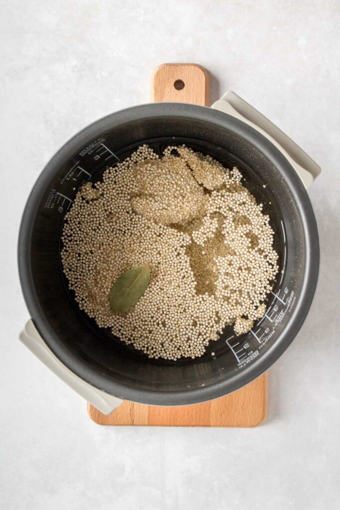 Quinoa with liquid, seasoning, and bay leaf in a rice cooker liner.