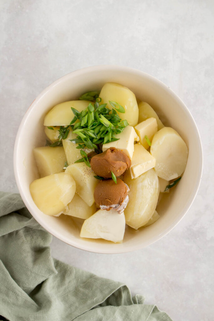 A bowl with miso, cream, green onions, and butter added to potatoes.