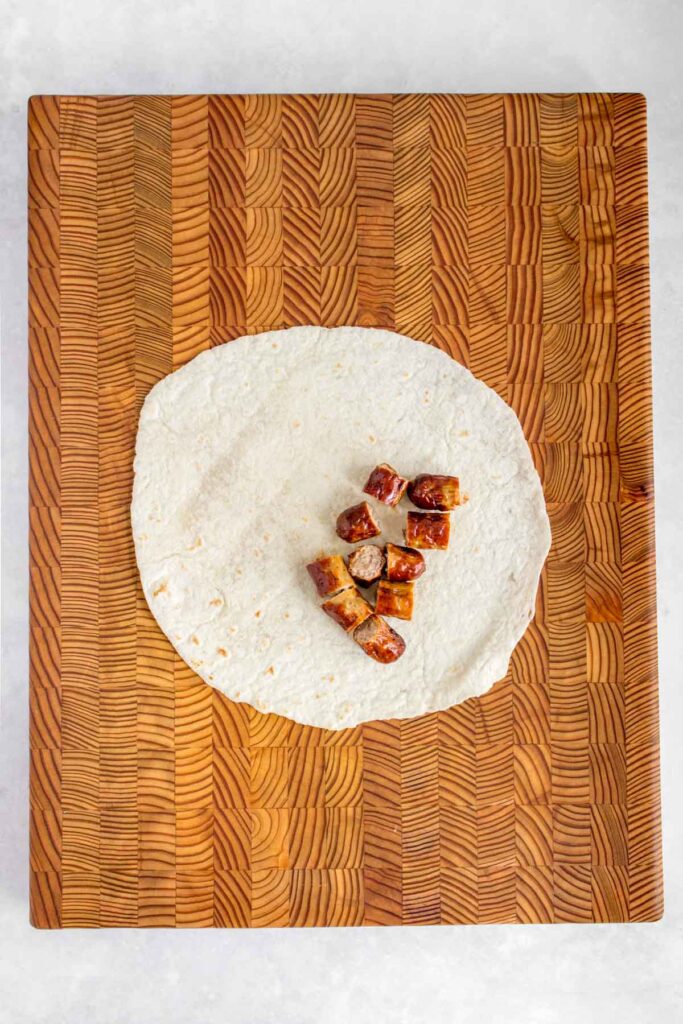 A tortilla wrap with cut sausages on a serving board.