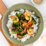 A bowl of rice with shrimp and broccoli on top.