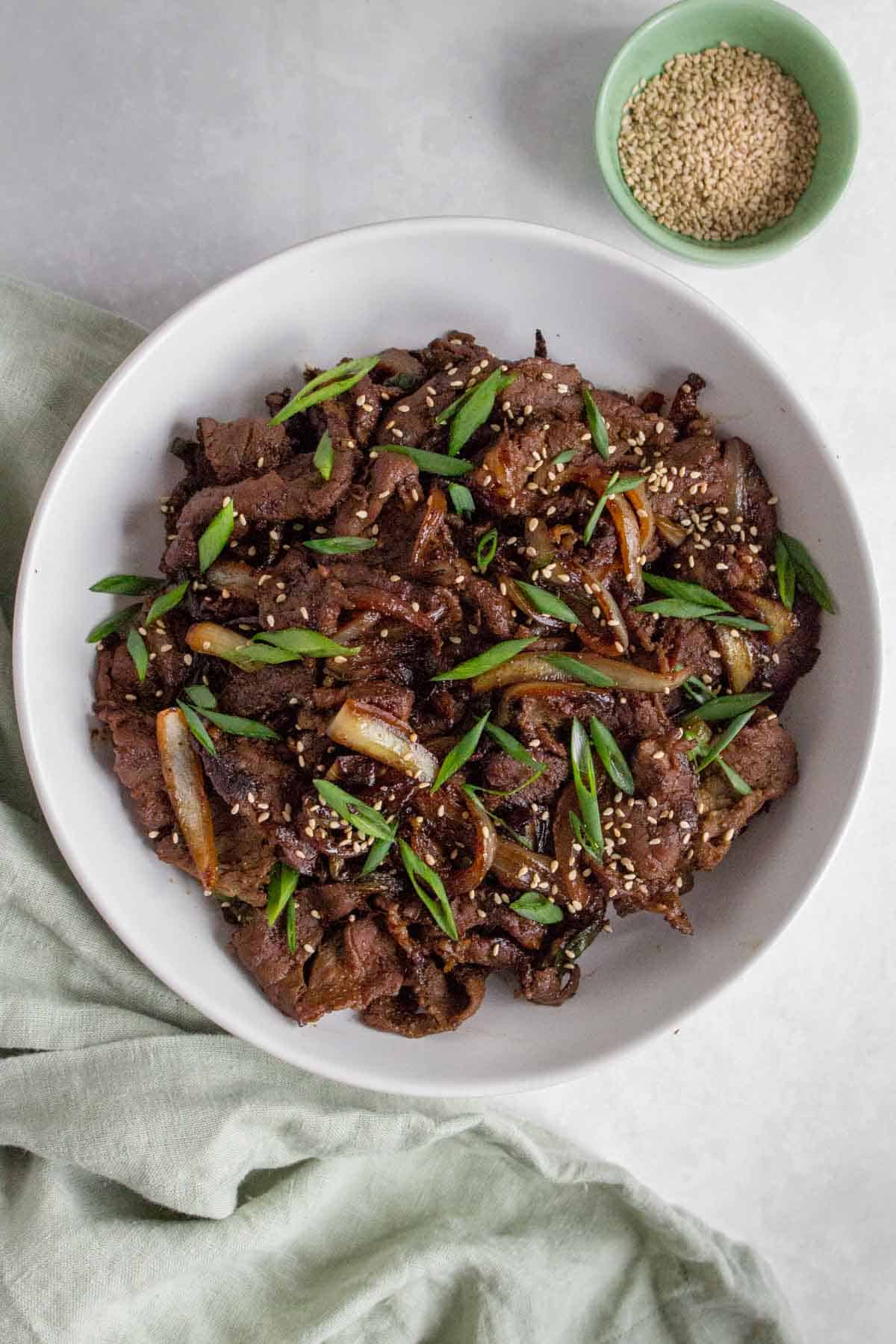 A large plate of beef bulgogi with green onions and sesame seeds on top.