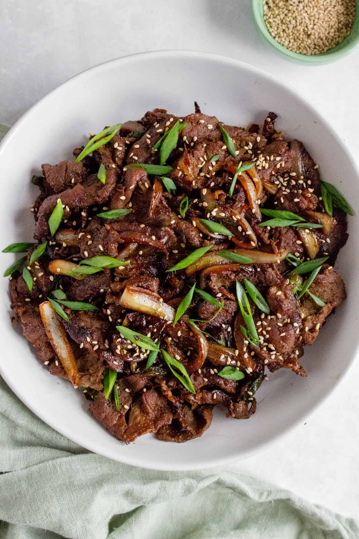 A large plate of beef bulgogi with green onions and sesame seeds on top.