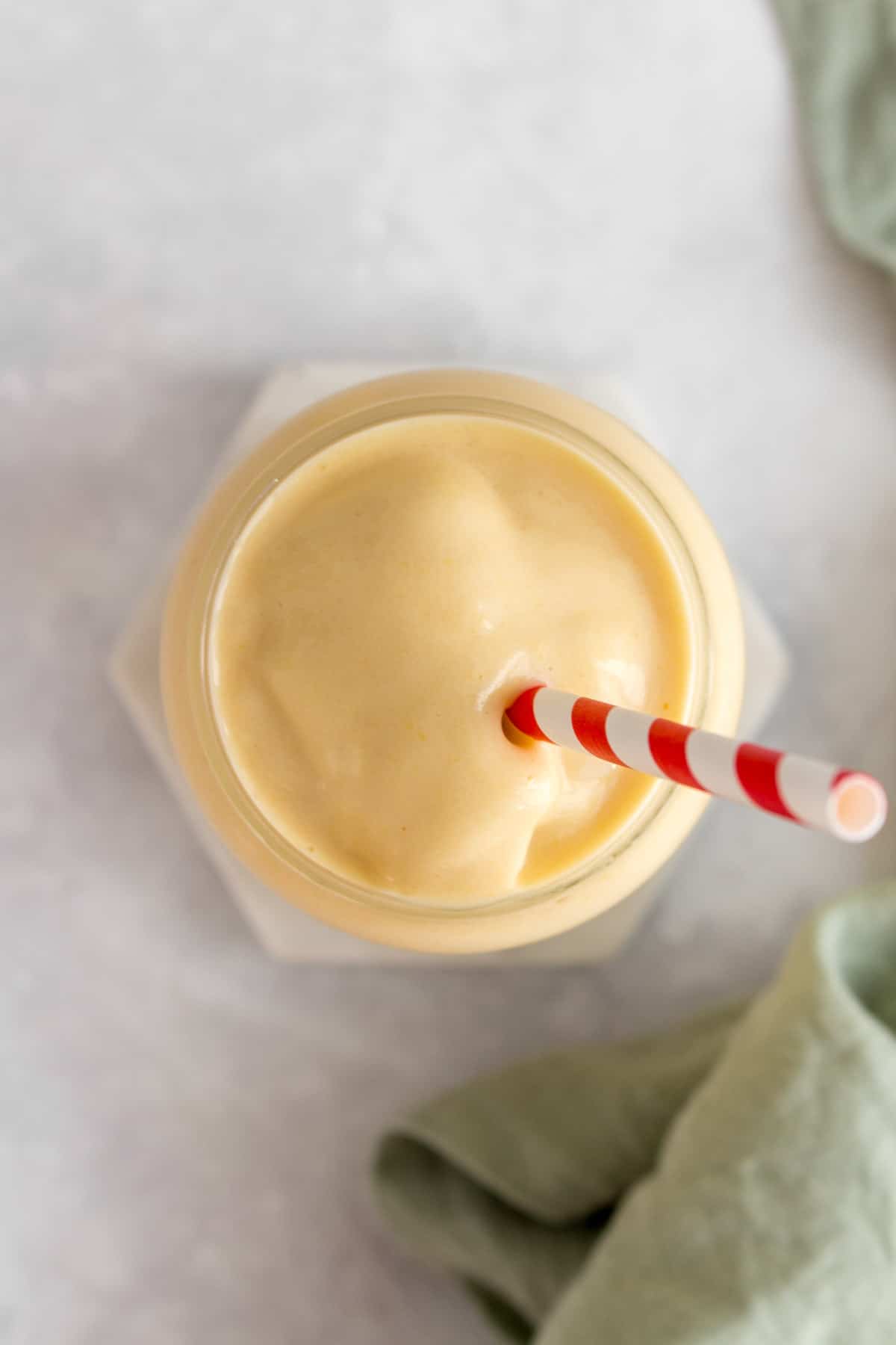 Overhead view of a glass of peach banana smoothie and a striped straw.