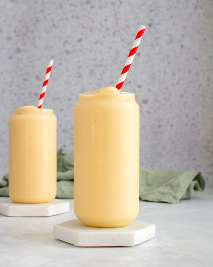Two tall glasses of peach banana smoothies, both with a striped straw.