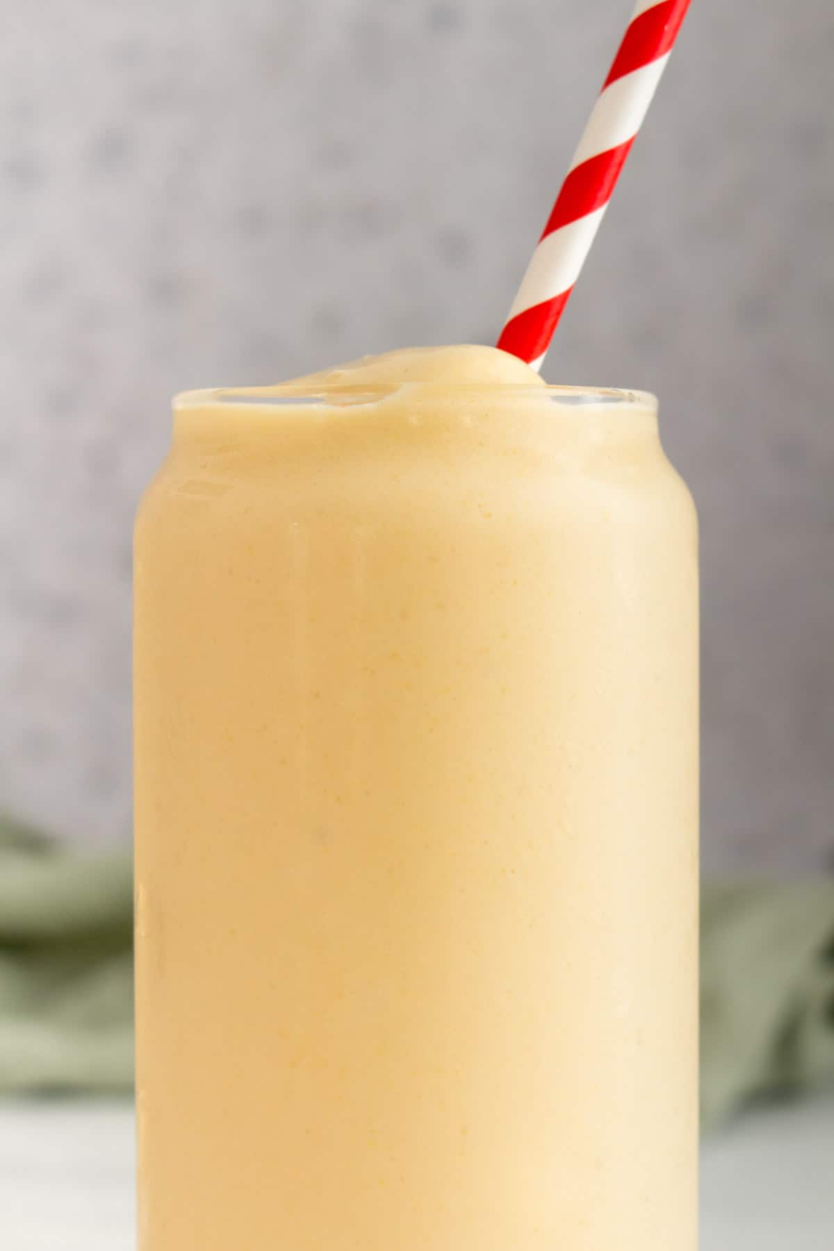 Close up of a glass of peach banana smoothie with a red and white striped straw.