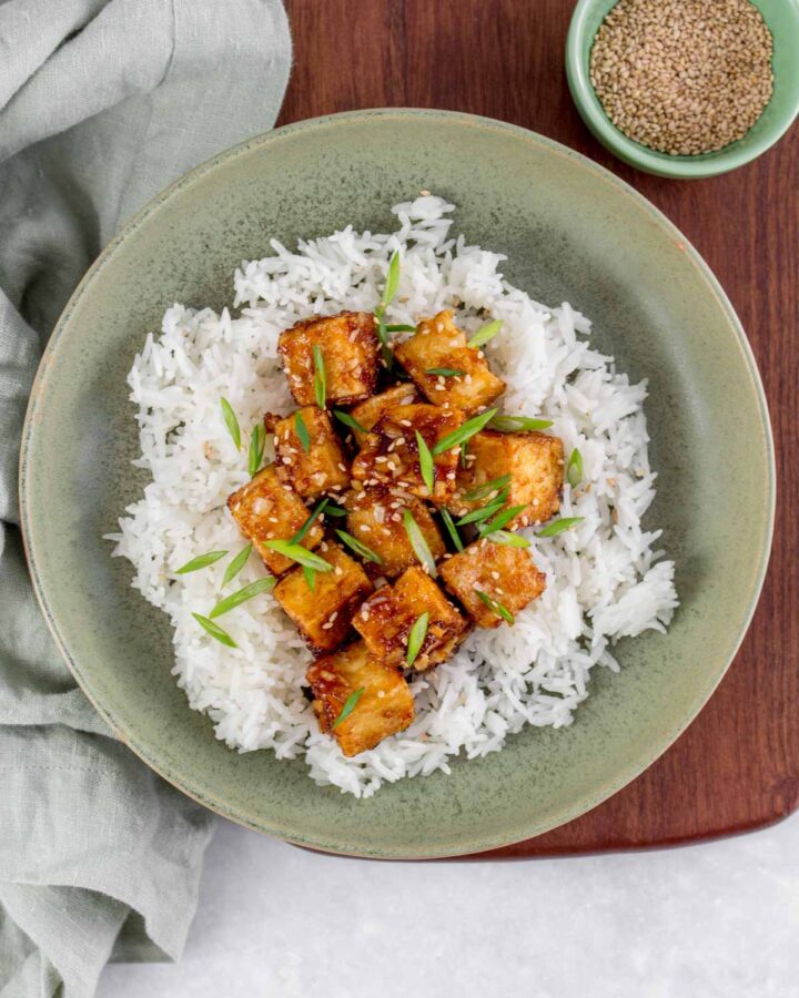 A bowl of rice with crispy pan fried sesame tofu on top.