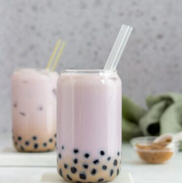 A glass of taro bubble tea with tapioca and a straw.