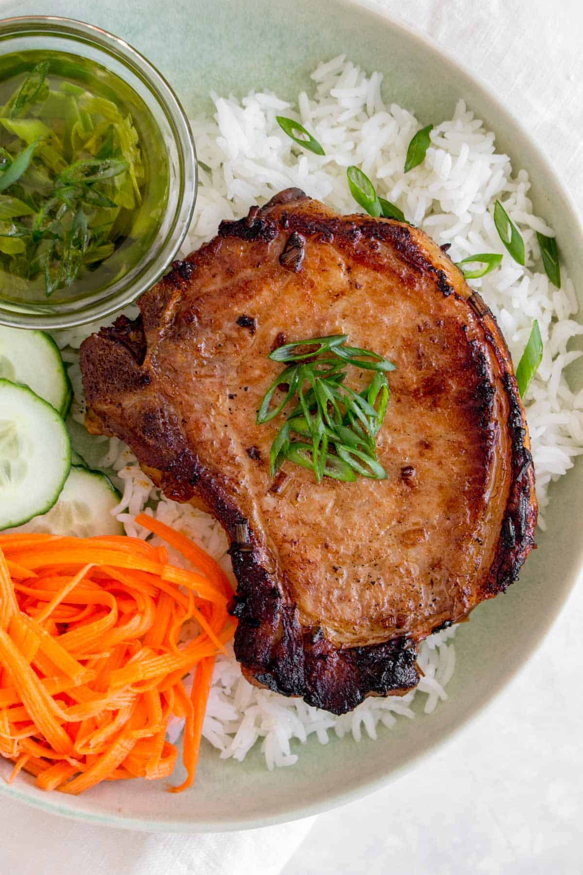 Close up of a Vietnamese pork chop over a bed of rice with scallions on top.