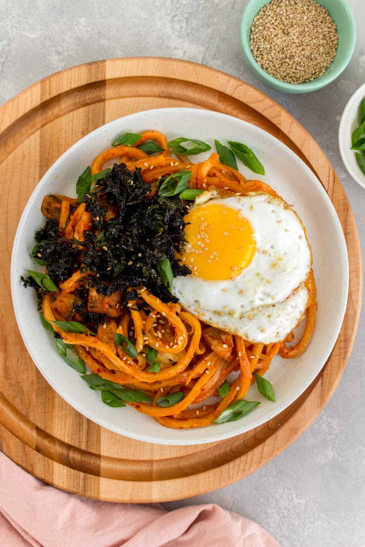 Overhead view of a plate of kimchi udon with a fried egg and seaweed on top.