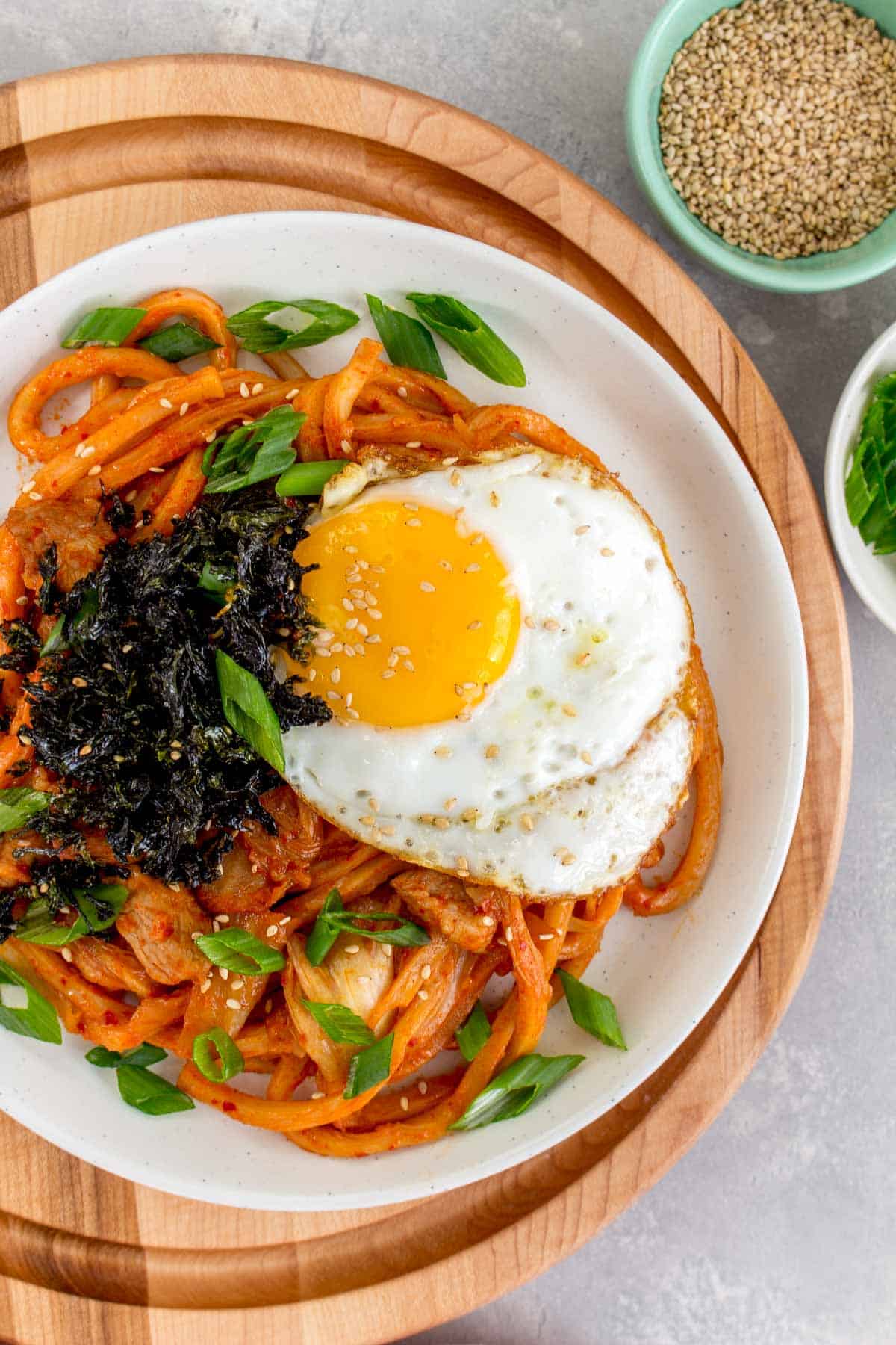 Close up of a plate of kimchi udon with a fried egg and seaweed.