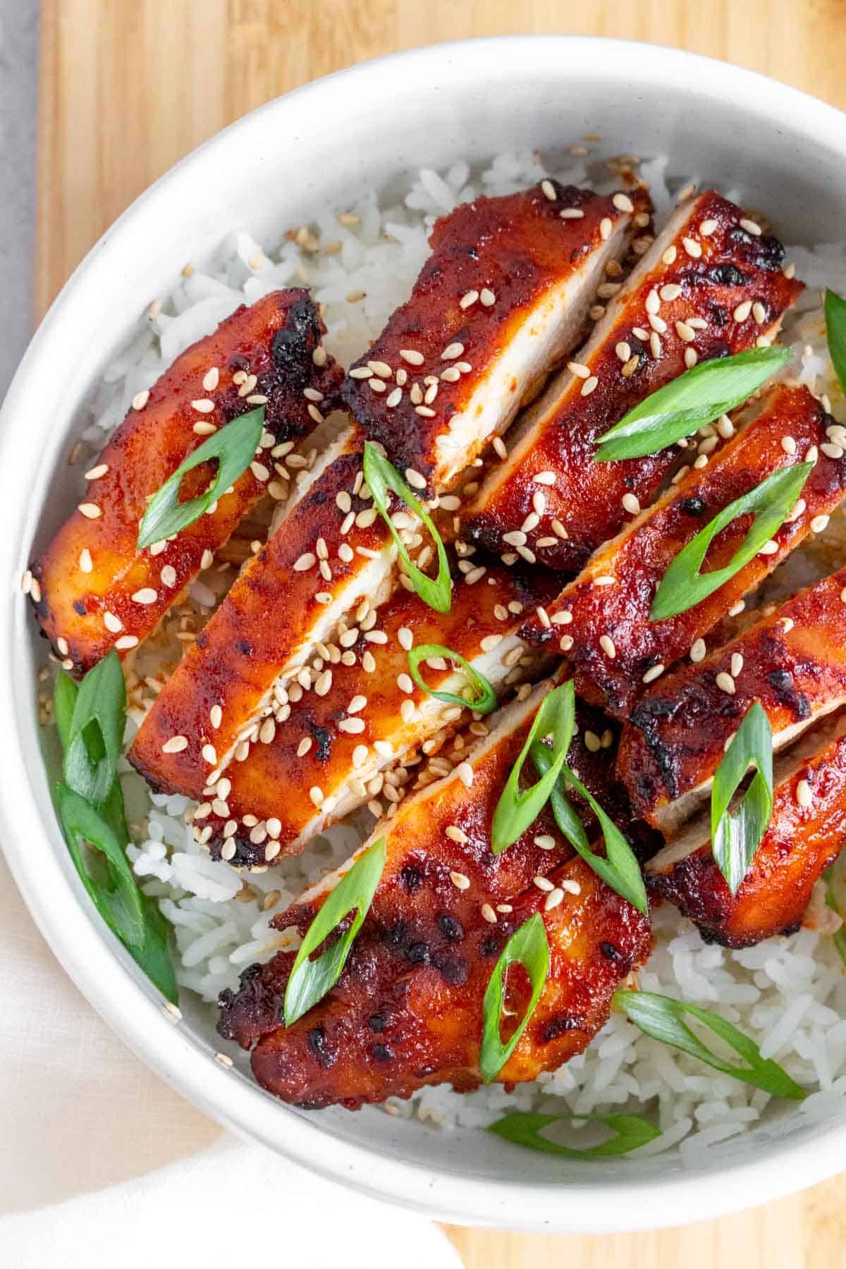 Close up of a bowl of rice with two sliced air fryer gochujang chicken thighs.