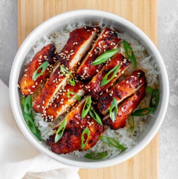 A bowl of rice with two sliced air fryer gochujang chicken thighs.