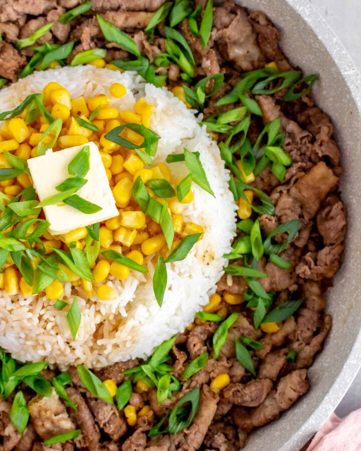 Close up of a dome of rice with corn, green onions, and butter on top, surrounded by stir fried beef.
