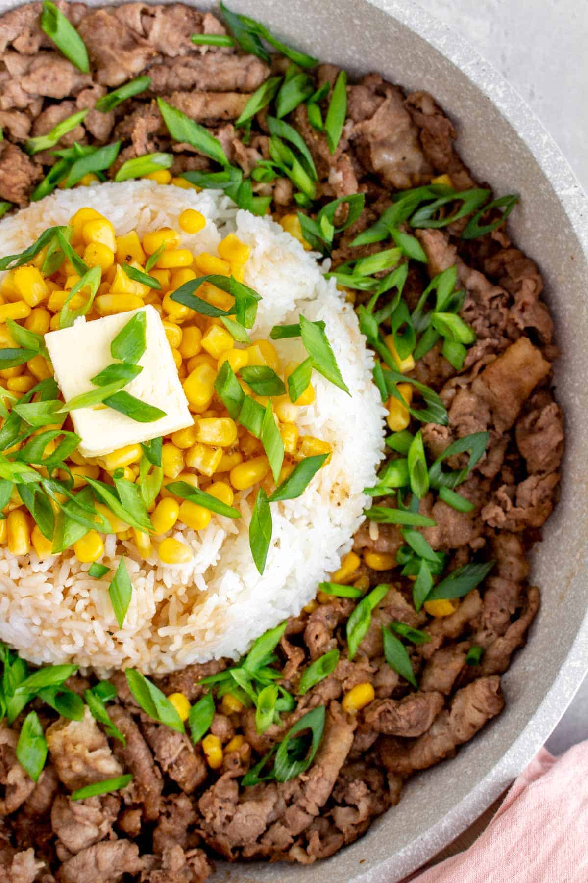 Close up of a dome of rice with corn, green onions, and butter on top, surrounded by stir fried beef.