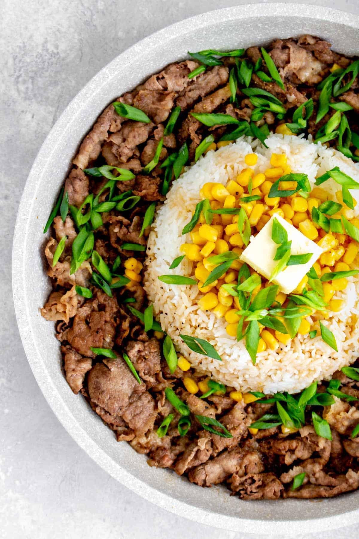 Close up of a dome of rice with corn, green onions, and butter on top, surrounded by stir fried beef.