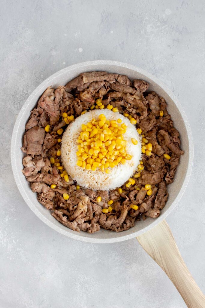 A pan of sliced beef with a dome of rice in the middle and corn on top.