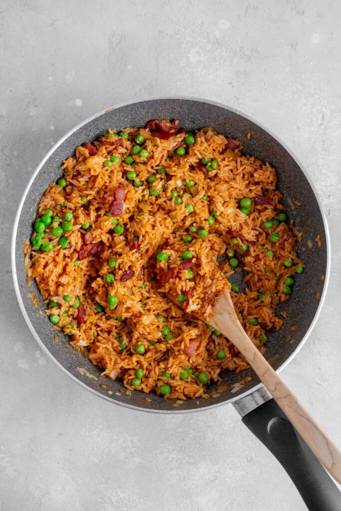 Peas and bacon added to the skillet of fried rice.