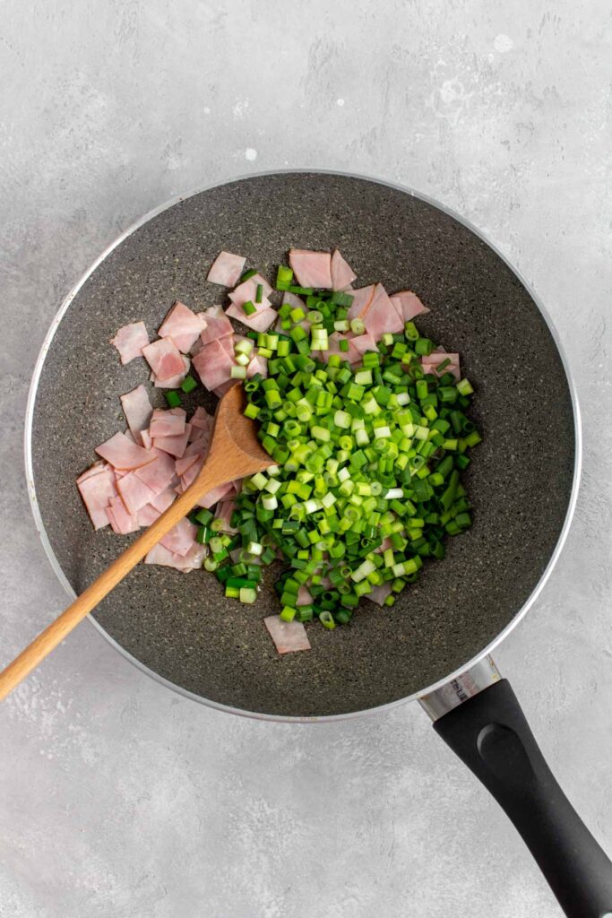 Ham and green onions added to a pan.