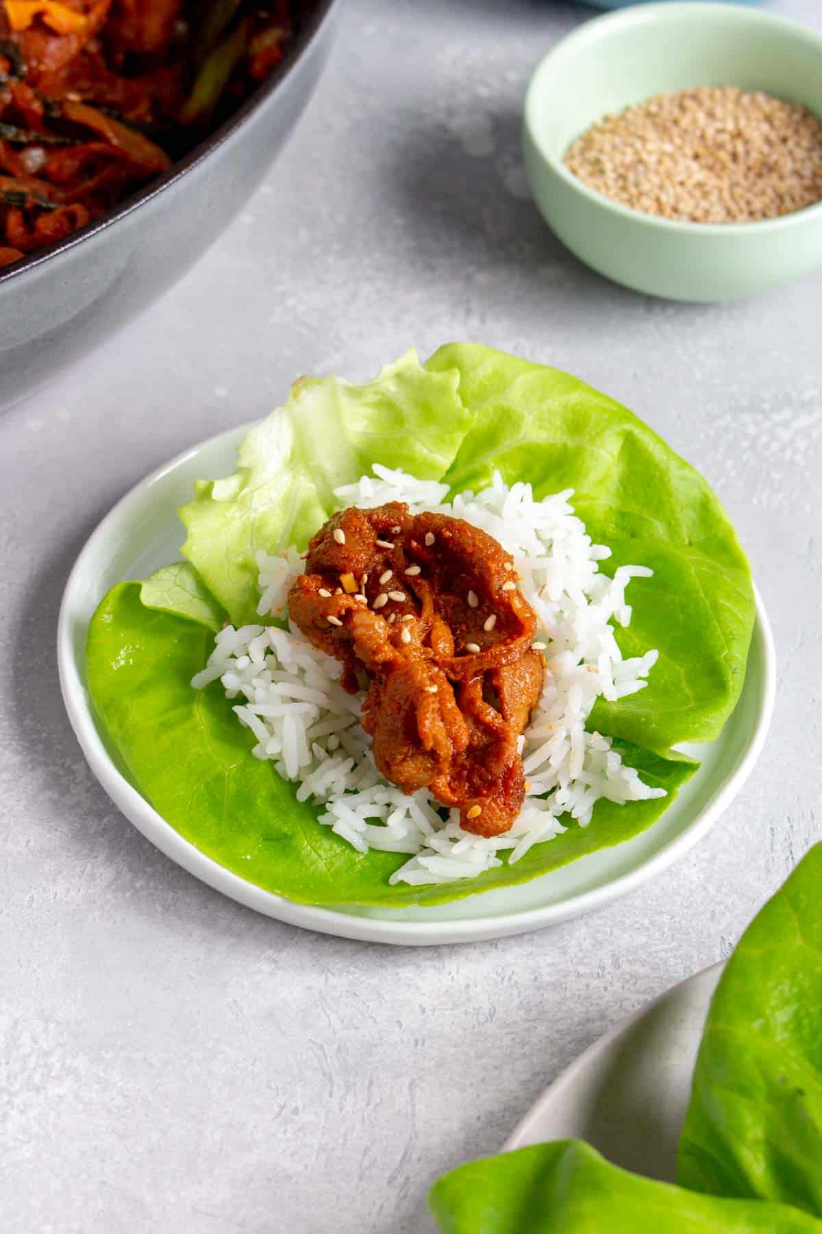 A plate with lettuce with rice and a piece of spicy pork stir fry.