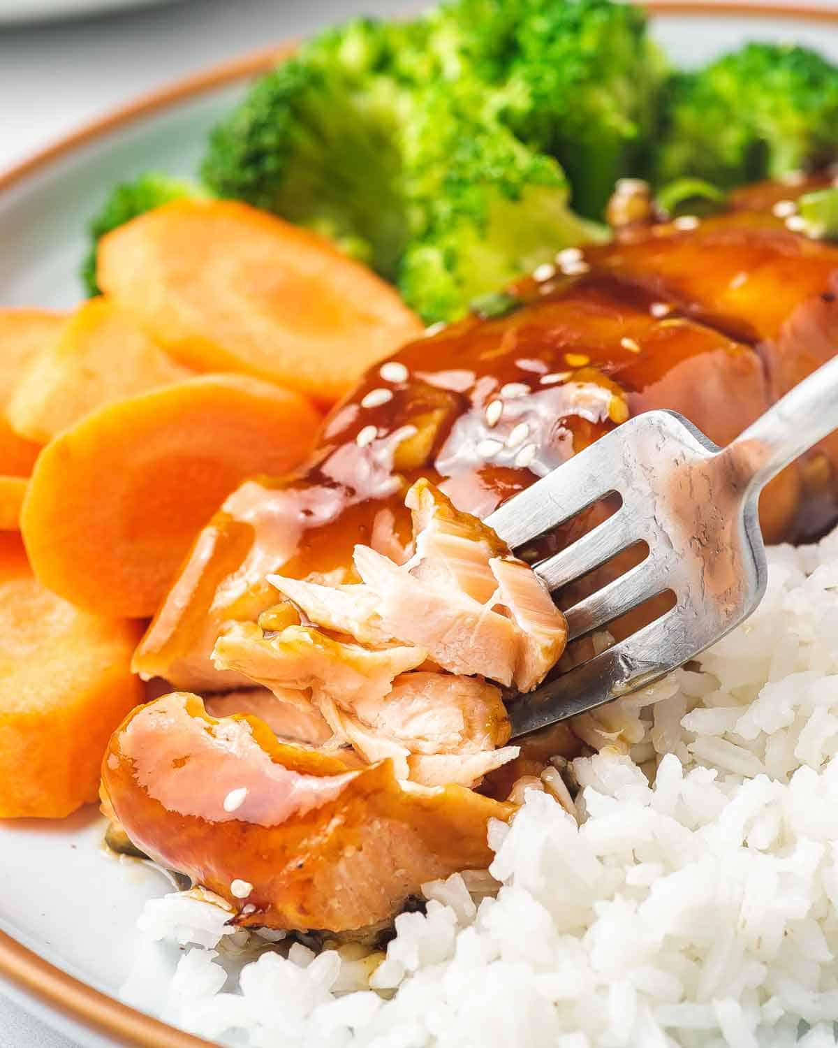 A fork flaking a piece of air fryer teriyaki salmon.