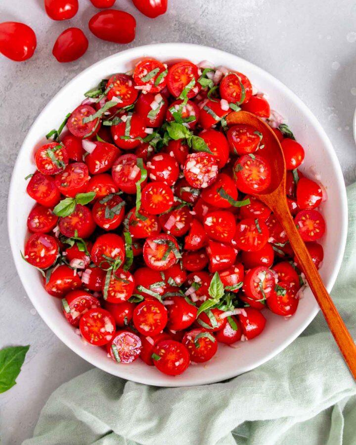A bowl of marinated tomatoes with a spoon inside.