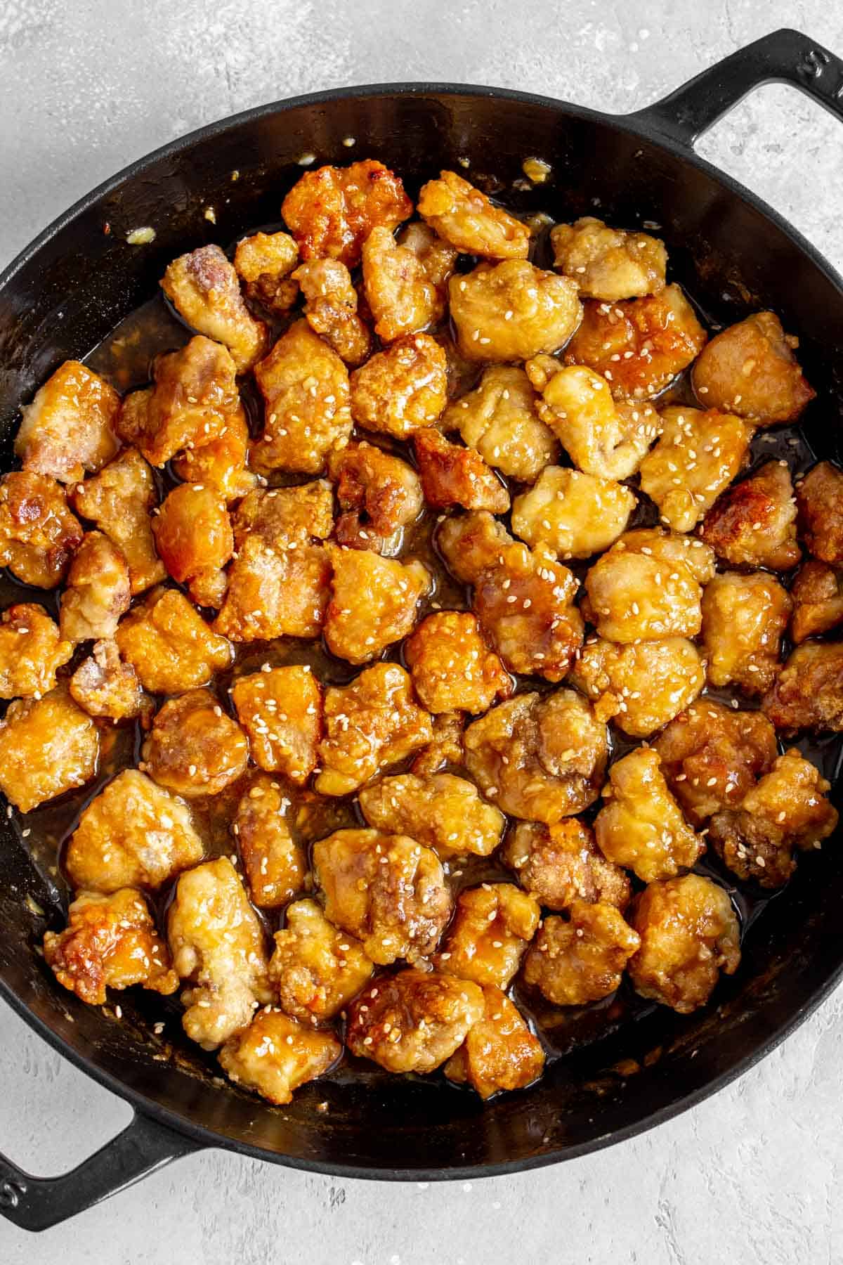 Close up of orange chicken in a large skillet with sesame seeds on top.