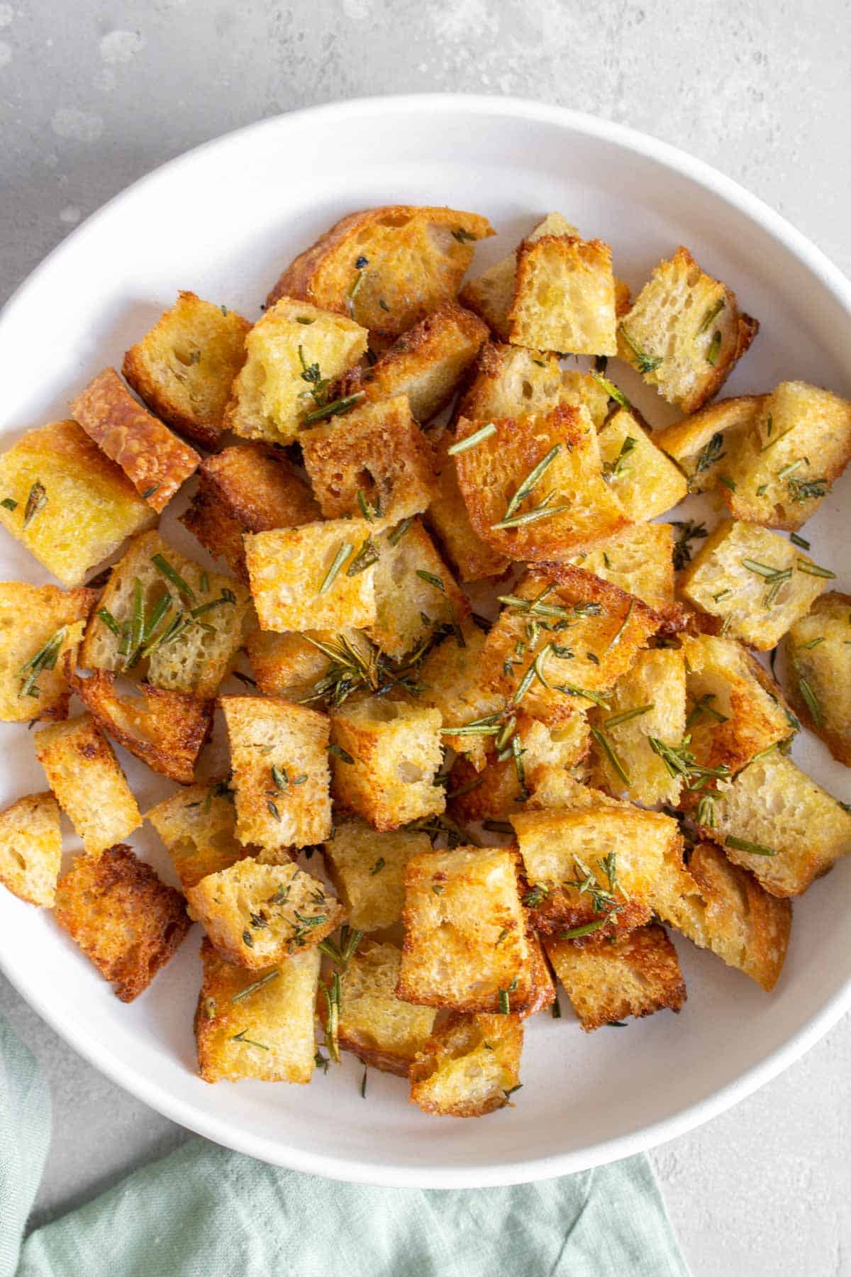 A white plate of air fryer croutons with rosemary and thyme.