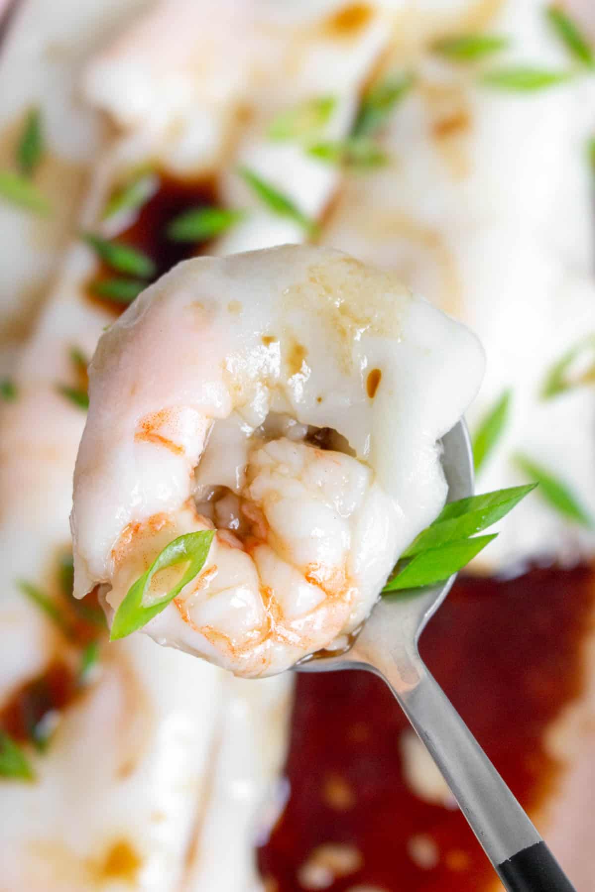 A spoonful of cheung fun with a piece of shrimp and green onions on top.
