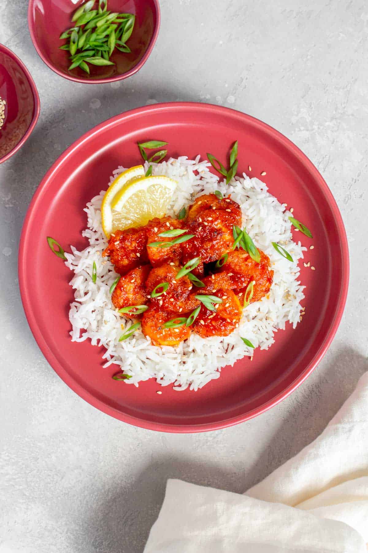 A plate of gochujang shrimp over rice with sliced lemon triangles.