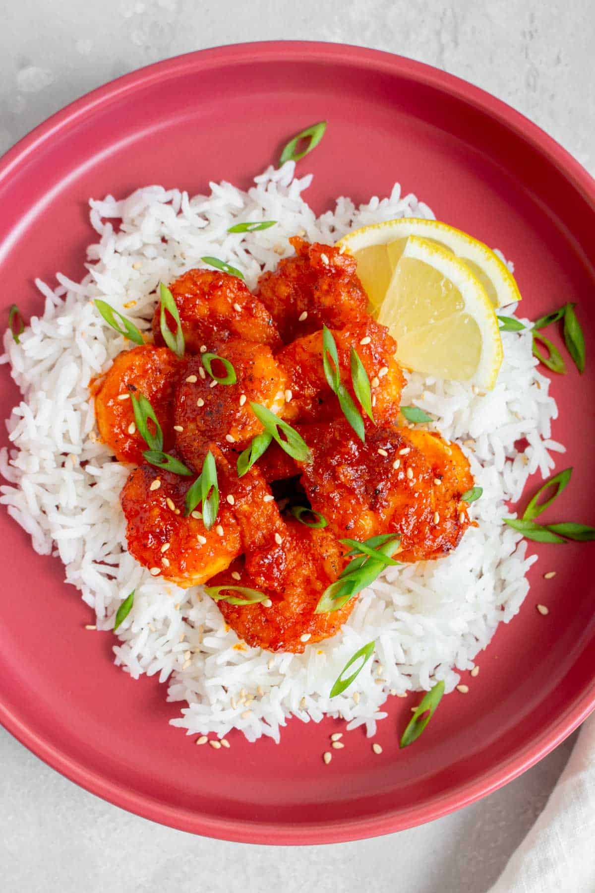 A red plate with rice, gochujang shrimp, and lemon triangles.