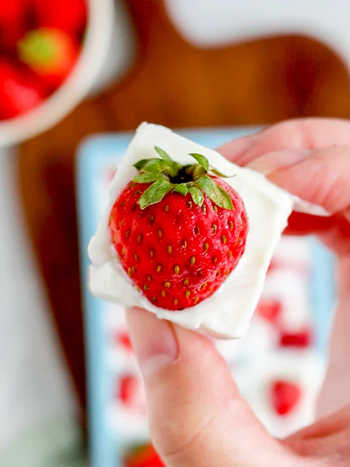 A hand holding up a cube of frozen yogurt with a strawberry.