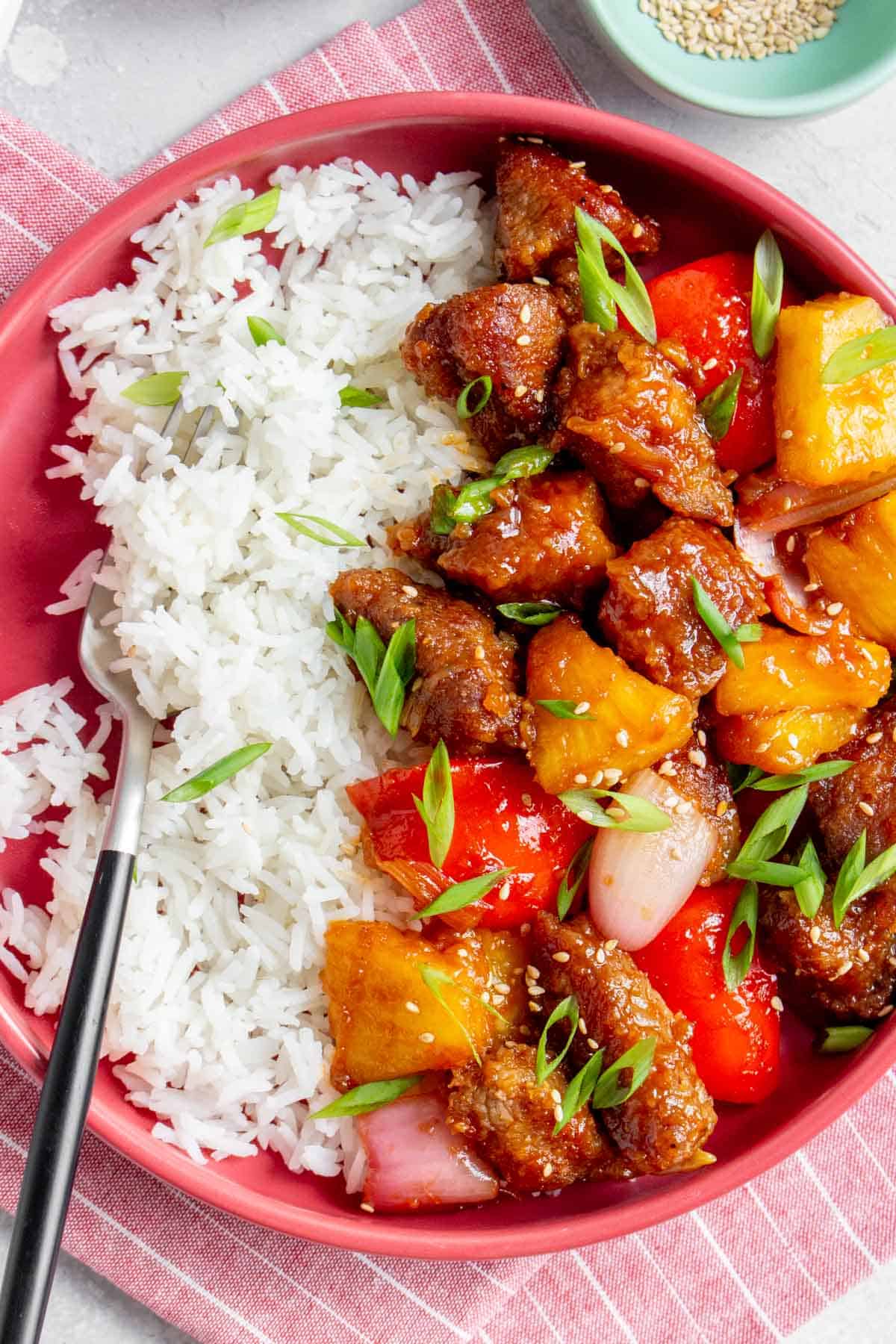A plate of sweet and sour pork with rice with a fork in the plate.