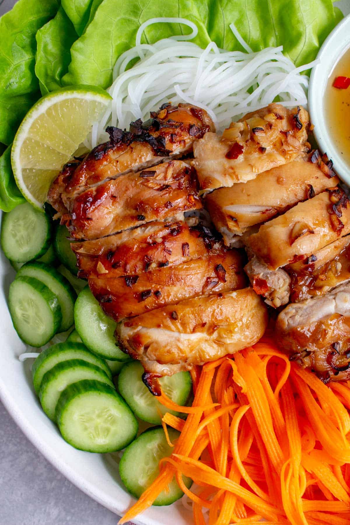 Close up of sliced air fryer lemongrass chicken thighs over some noodles, cucumber, and pickled carrots.
