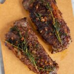 Overhead view of two garlic butter steaks with rosemary.