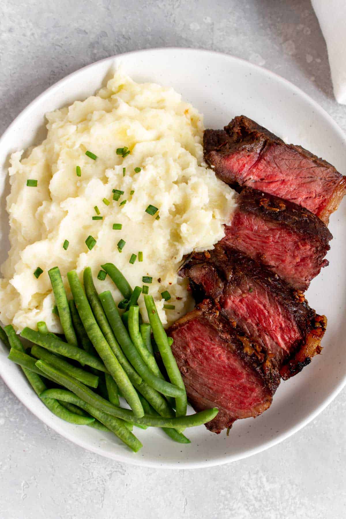 A plate with mashed potatoes, green beans, and sliced steak.