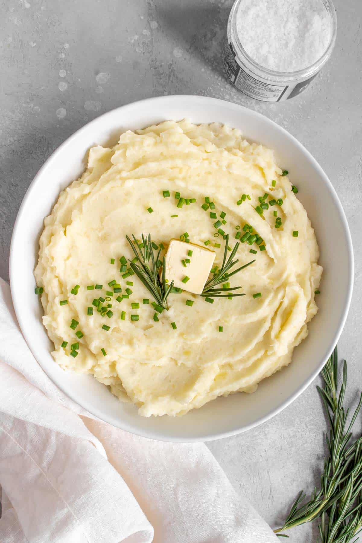 A bowl of rosemary mashed potatoes with butter, chives, and rosemary.