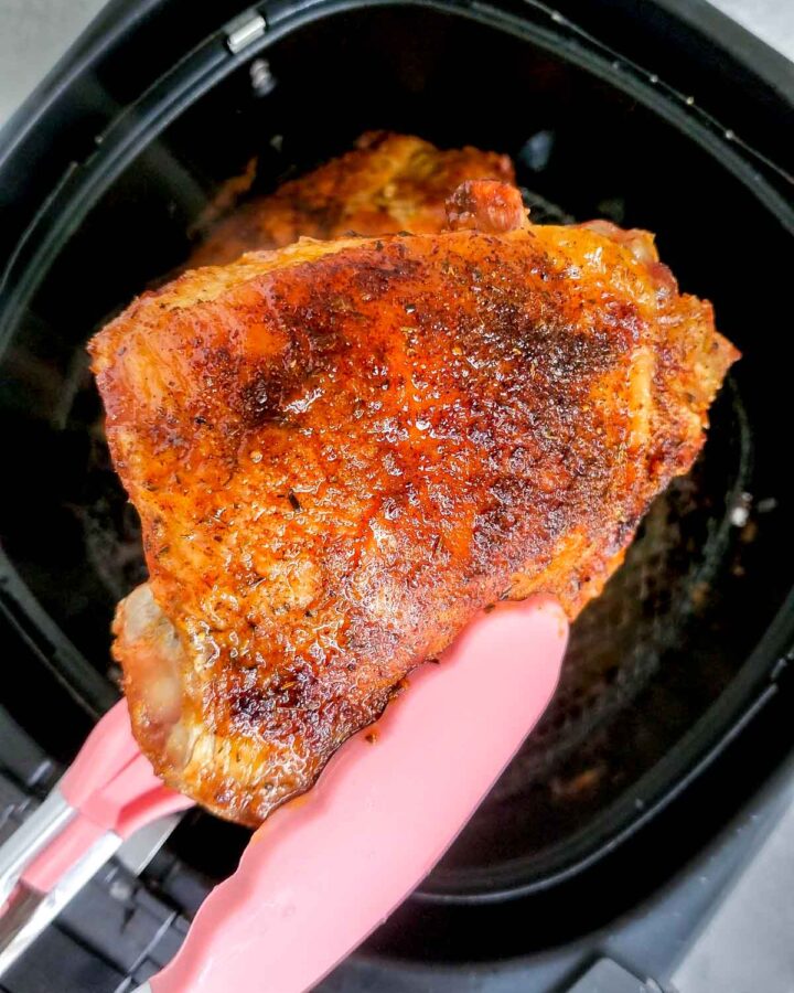 An air fryer turkey thighs lifted up with tongs from an air fryer basket.