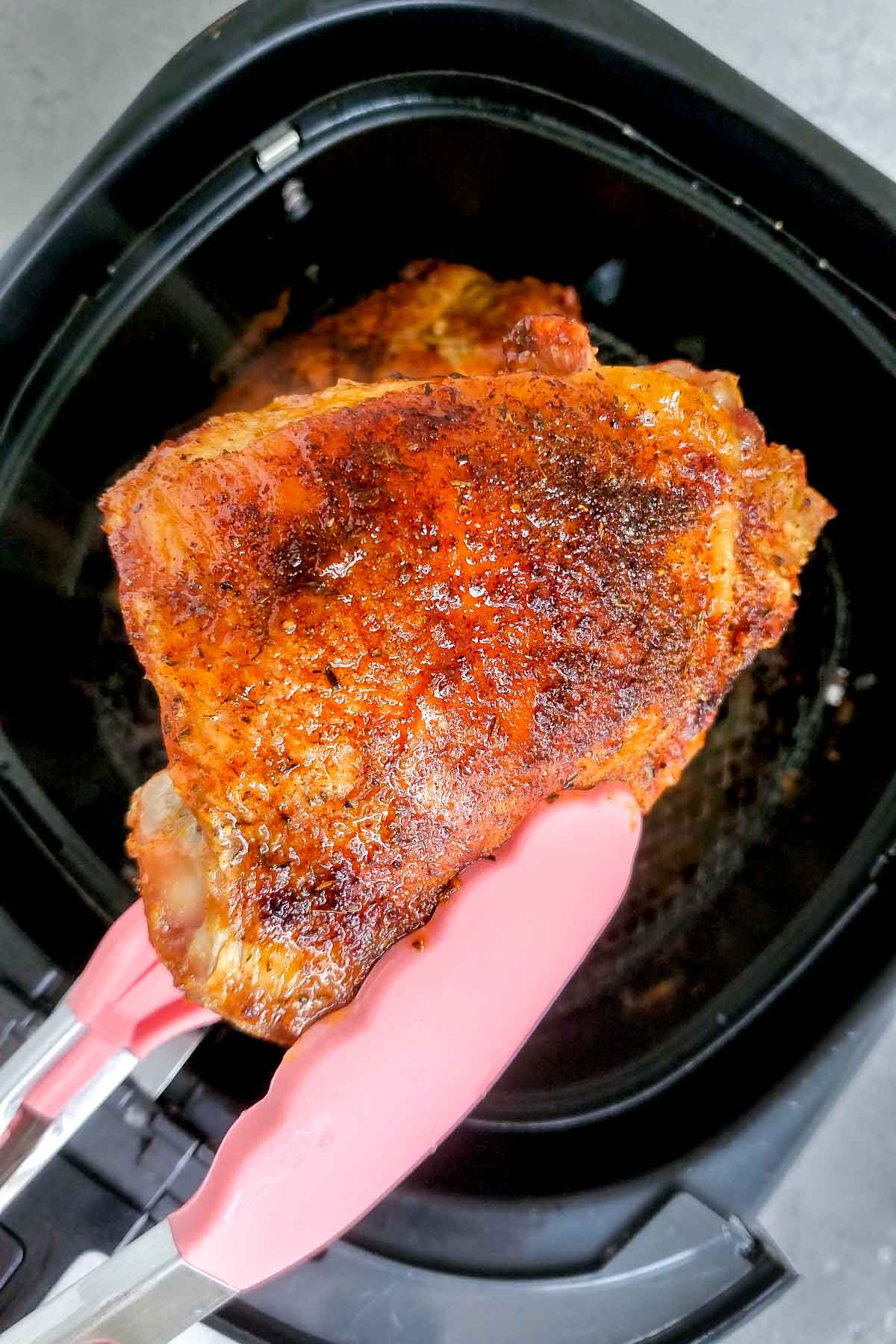An air fryer turkey thighs lifted up with tongs from an air fryer basket.